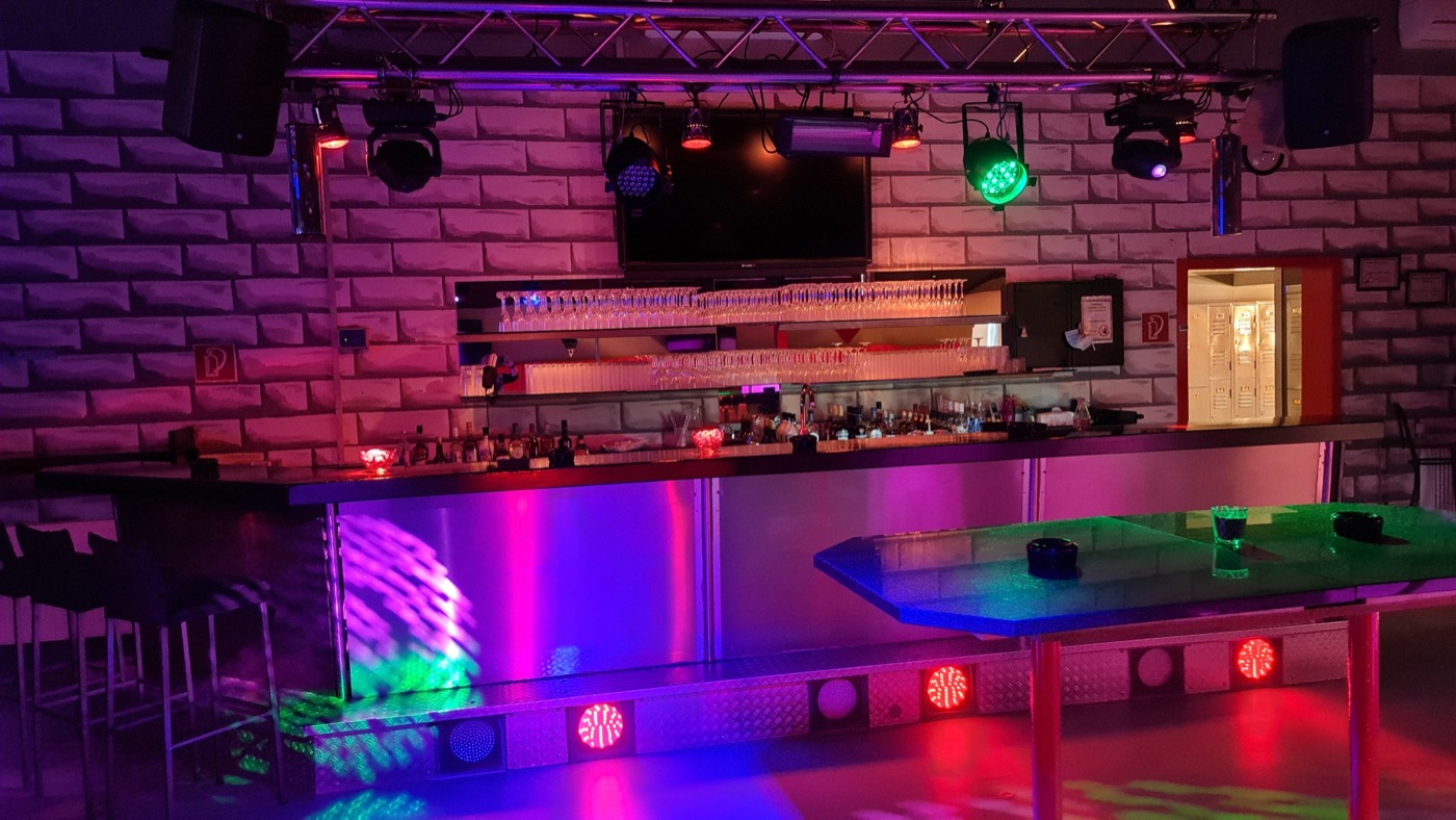 Bar mit Gläserregal, Flaschen und Lichtanlage.