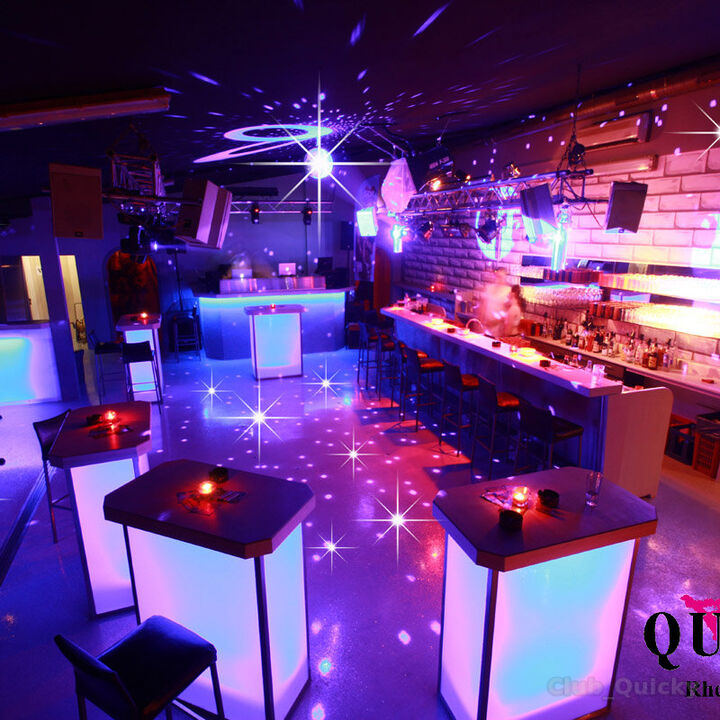 Partyraum mit Bar, beleuchteten Tischen und Lichtanlage.