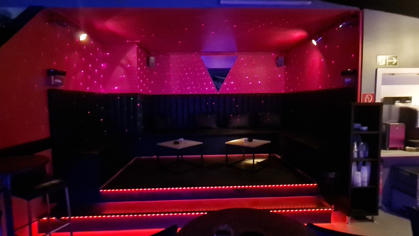 Sitzecke im Partyraum mit roter Beleuchtung und zwei Tischen.