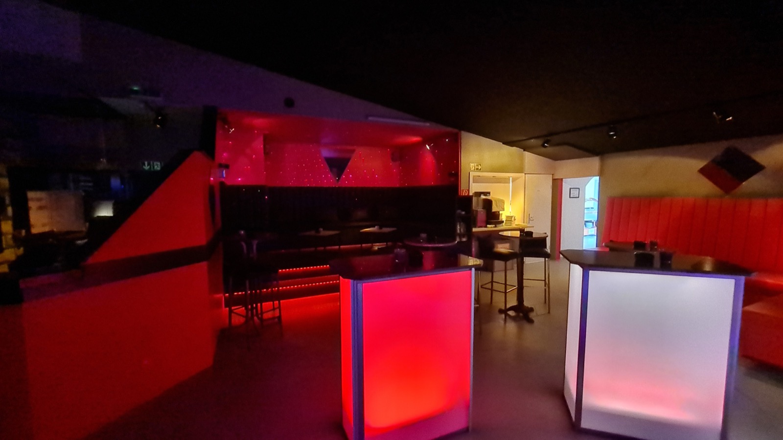 Partyraum mit leuchtenden Stehtischen und roter Sitzecke.